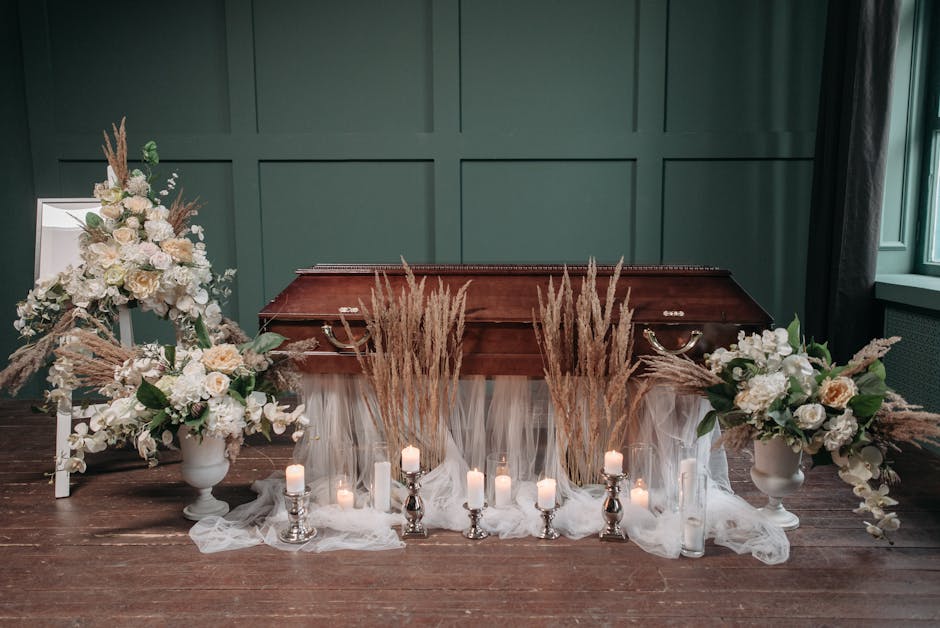 A floral arrangement composed of white and cream roses, hydrangeas, and other soft blooms, accented with beige pampas grass and green foliage, is displayed in elegant white vases on either side of a p
